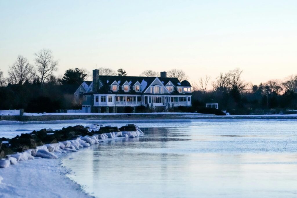 A serene winter scene of a waterfront mansion at sunset, surrounded by icy waters.