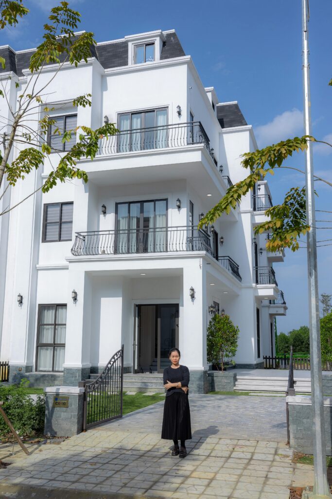 Contemporary white house exterior with a woman standing in front, clear blue sky.
